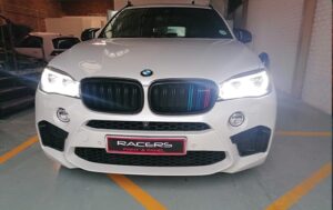 Picture shows a white BMW with headlights on inside the entrance of Racers workshop after having undergone Auto body repair at Racers Paint and Panel